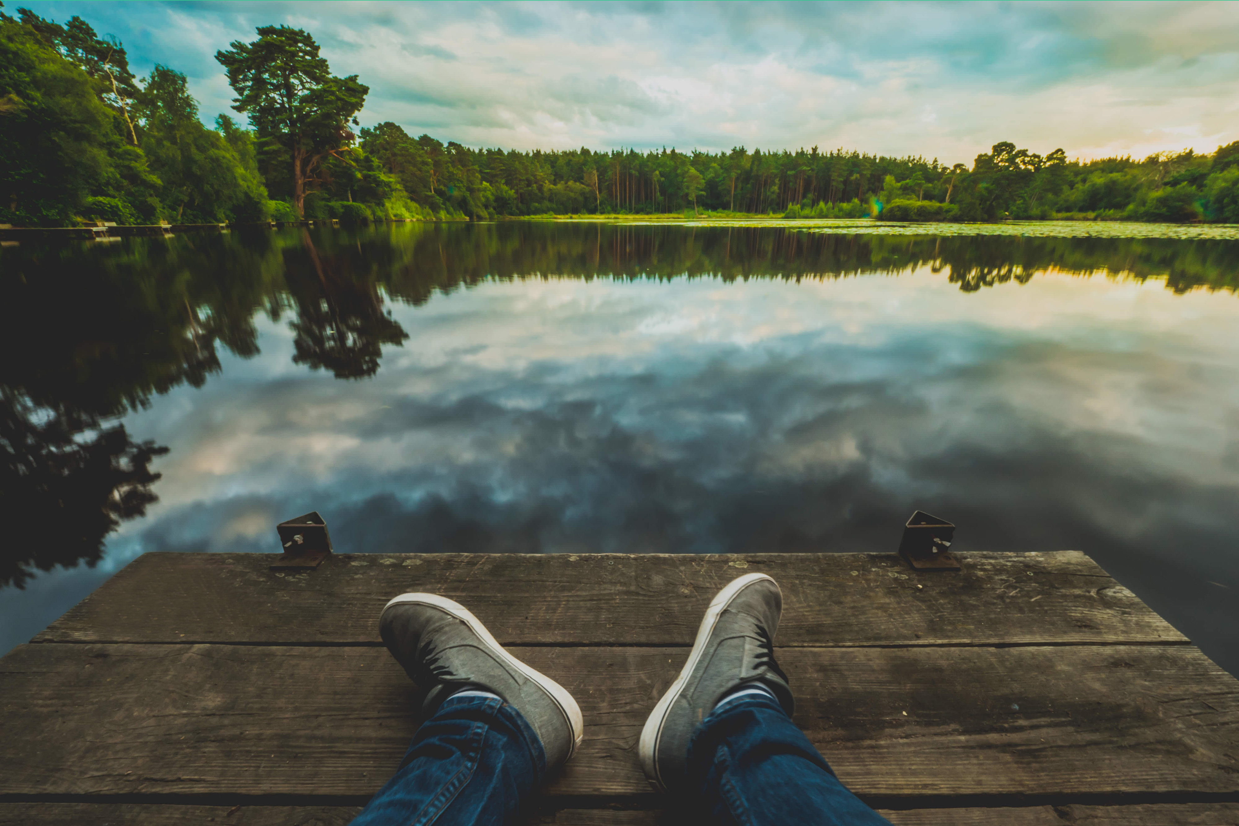 A man sits on a dock by a calm lake surrounded by trees, looking relaxed and peaceful. The image conveys a sense of serenity and introspection. This image may be relevant to Cognitive Behavioral Therapy in Connecticut, as CBT often involves mindfulness exercises and relaxation techniques to manage symptoms.