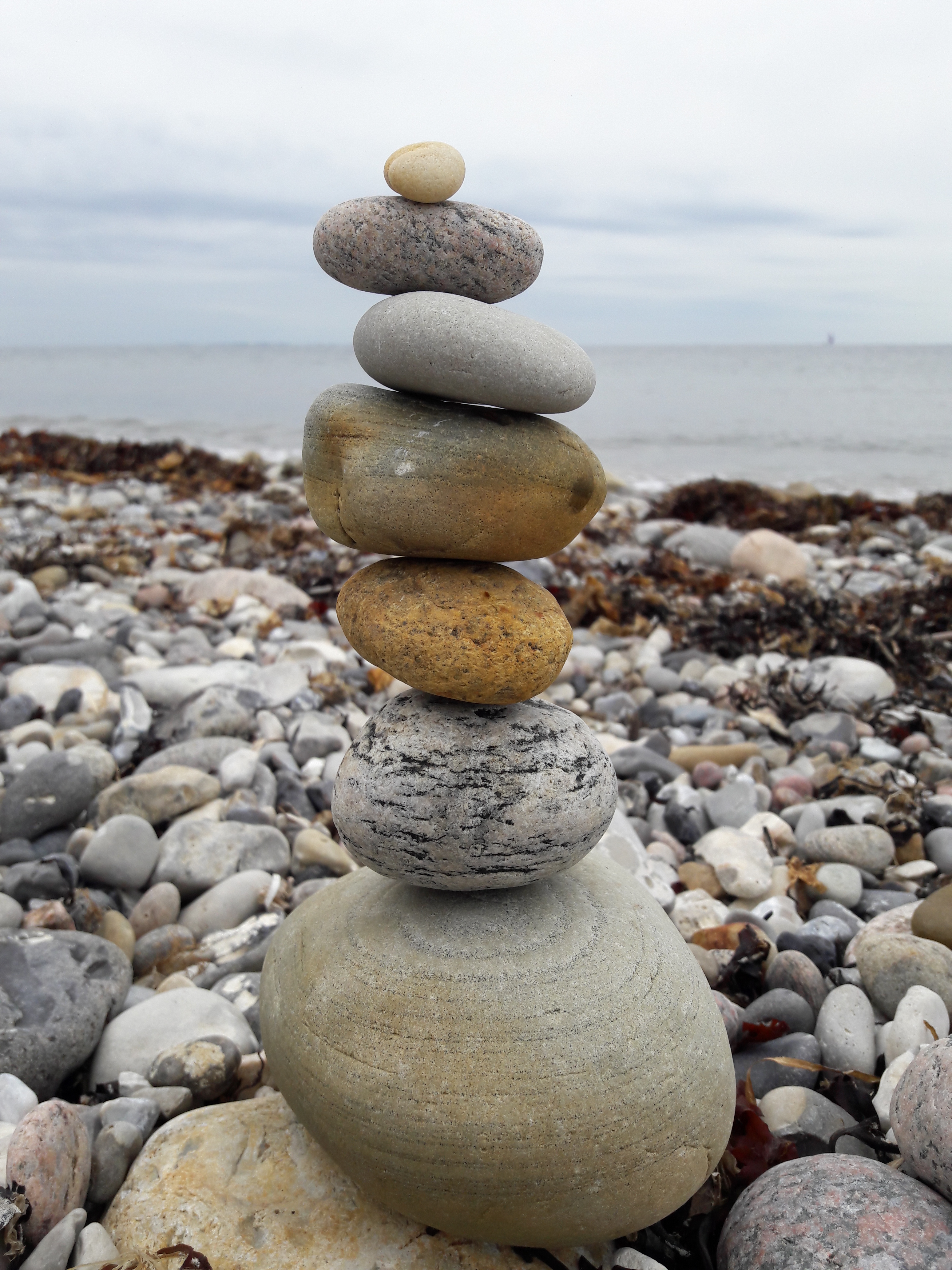 The photo depicts a group of smooth, flat stones stacked atop each other on a sandy beach. The stones vary in shades of gray, brown, and tan, and are arranged in a way that suggests harmony and balance. Some stacks are simple, while others are more elaborate and intricate. This image evokes a sense of peace and tranquility, and could be associated with activities like mindfulness practice, meditation, or contemplative therapy such as DBT therapy in CT.