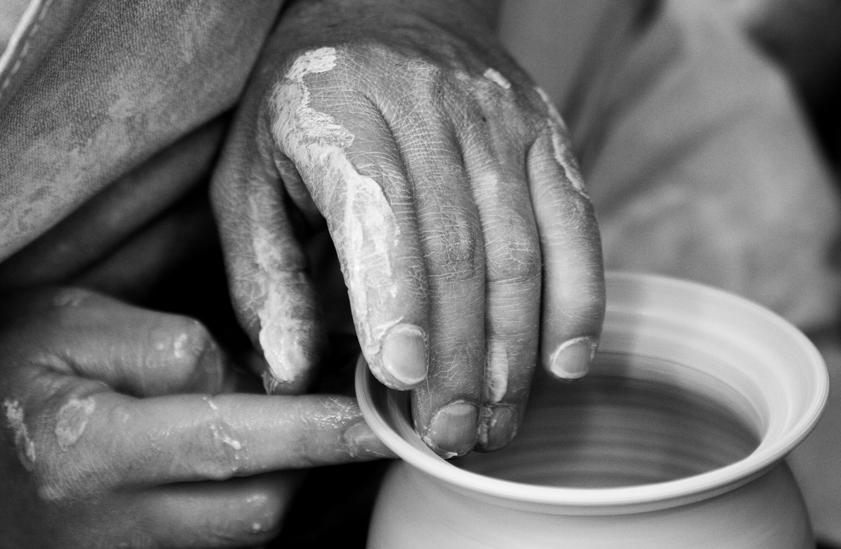 A photo of a person's hands shaping a piece of pottery on a pottery wheel. The clay is wet and messy, and the potter's hands are covered in it. The pottery wheel is turning, and there are tools and other pots visible in the background. This image could relate to the therapeutic process of DBT therapy in Connecticut, which can involve molding and shaping new ways of thinking and behavior.